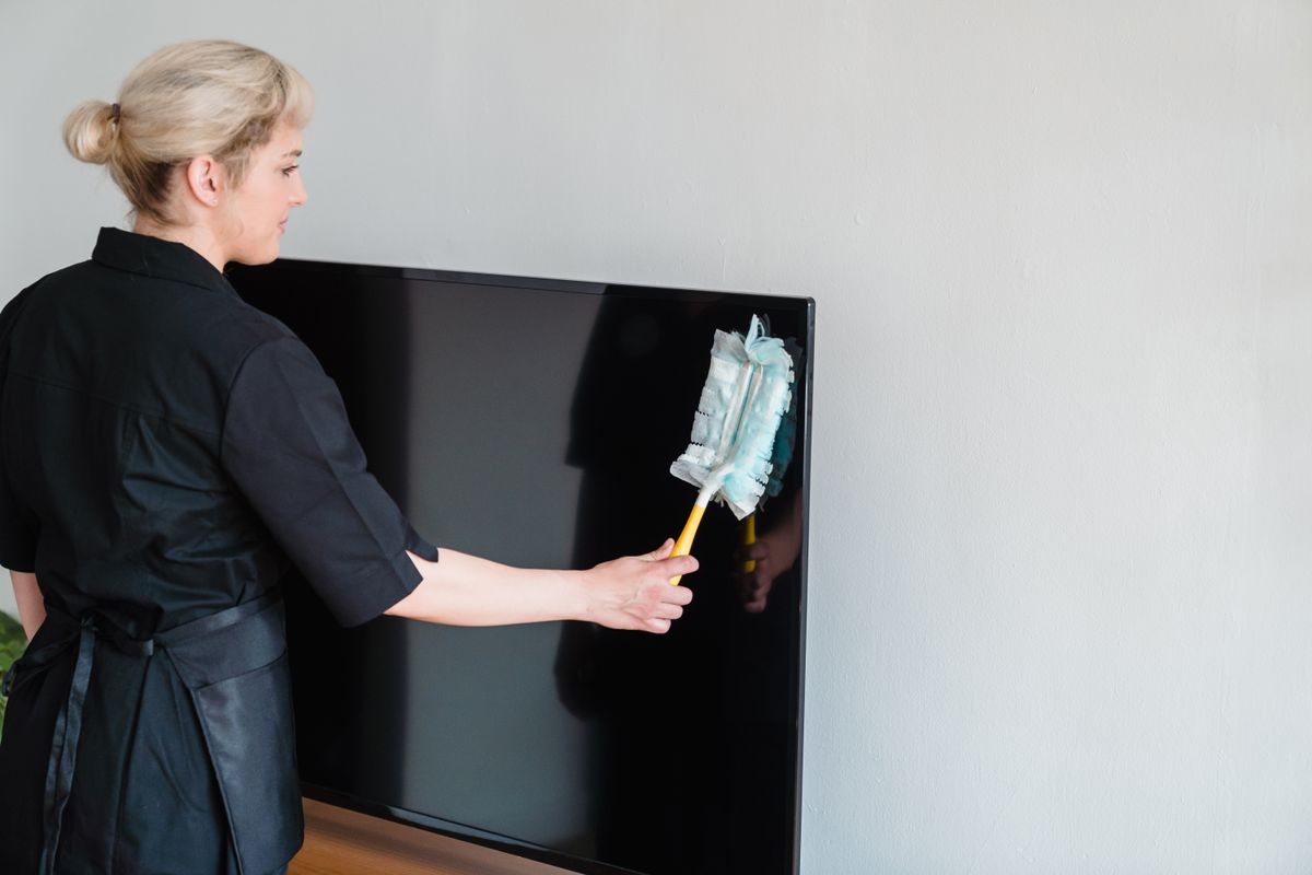 Housekeeper carefully dusting a screen and surfaces in a living room