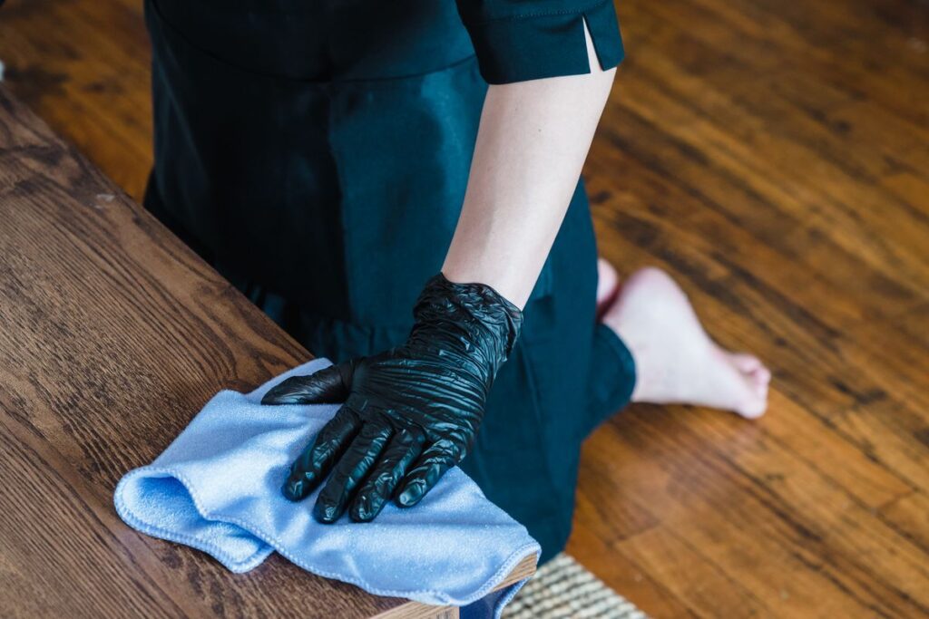 Professional house cleaner wearing gloves wiping down a wooden table with a cloth