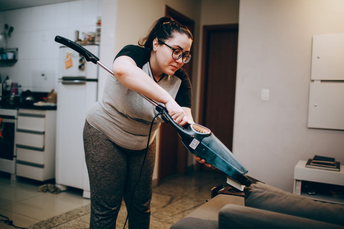 Cleaner vacuuming a fabric sofa in a comfortable living room