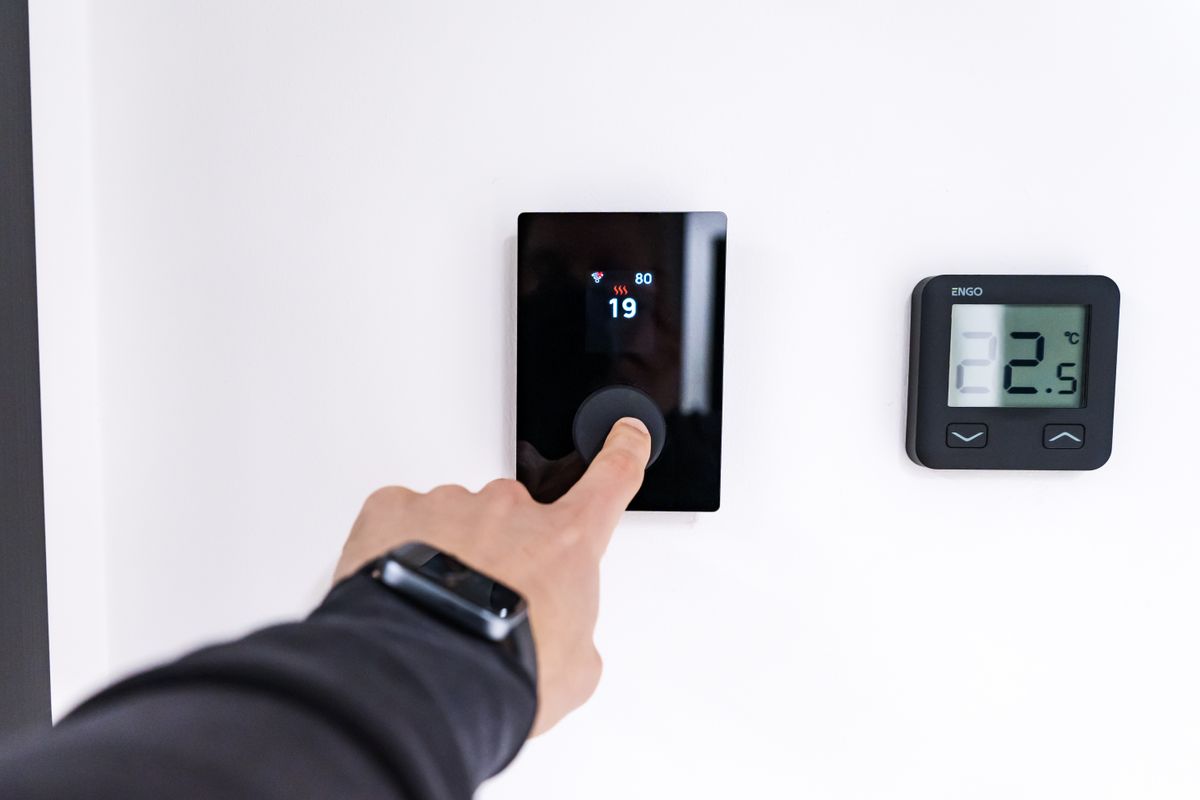 Hand adjusting a digital thermostat on the wall of a modern home