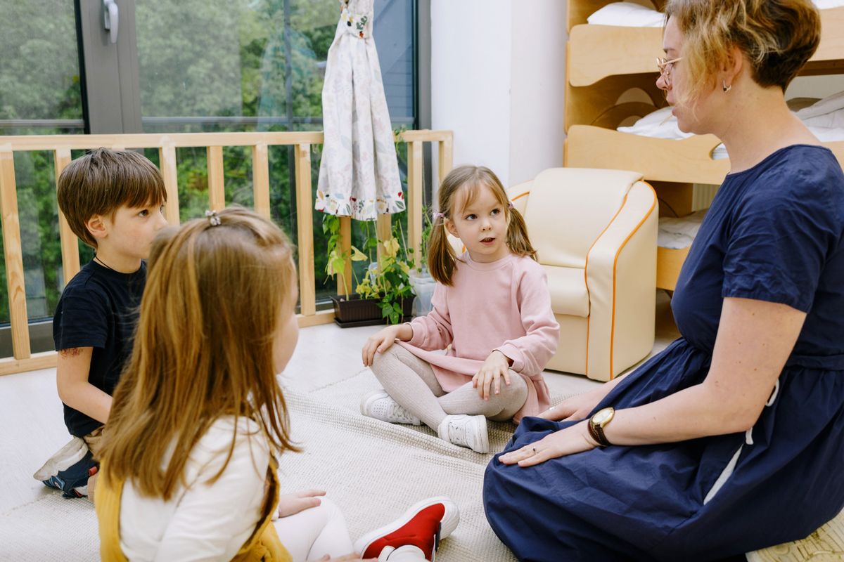 An adult sitting on the floor talking with children during a childcare visit