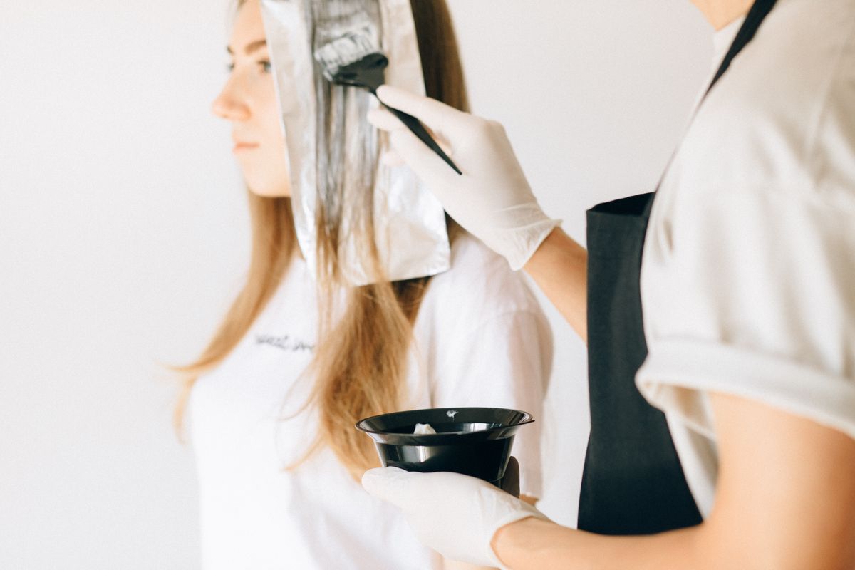 Hairdresser applying colour to a client's hair using a brush and foils