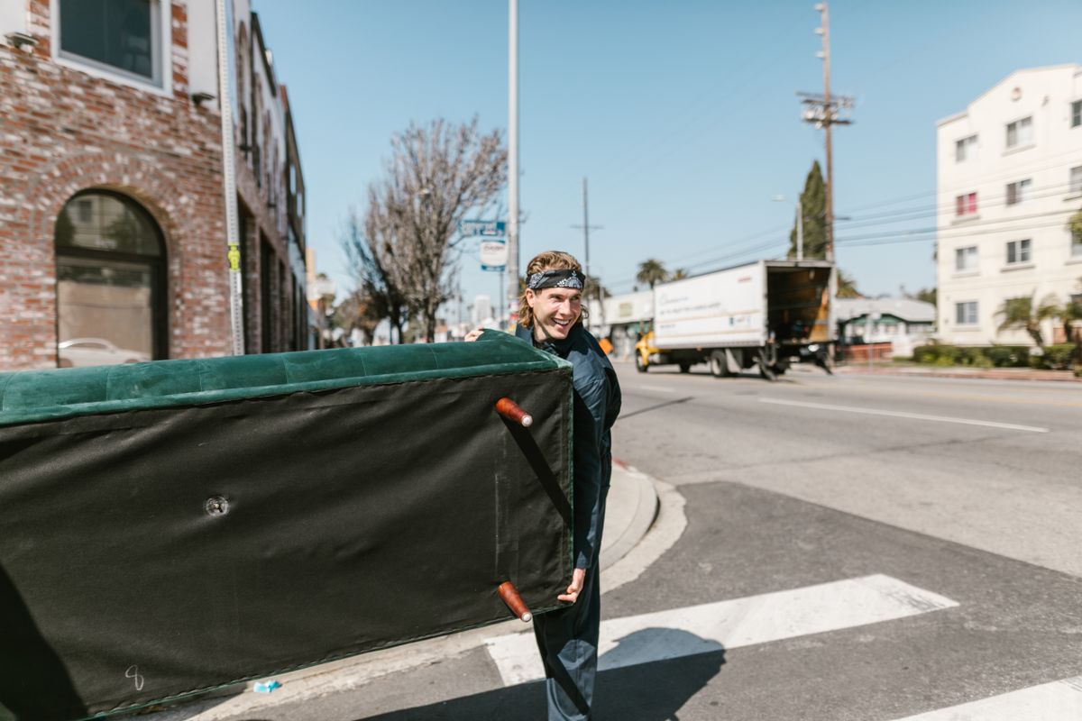 Mover carrying a large sofa along a street during a house move