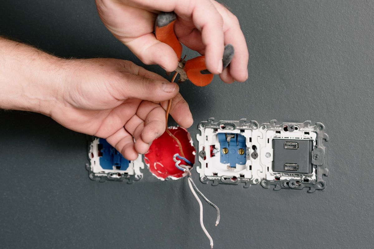 Electrician using pliers to wire a power socket into a wall during a home job