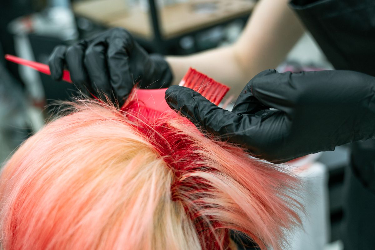 Close-up of gloved hands applying hair dye during a salon colour service