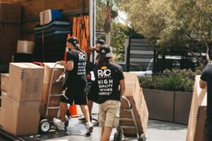 Movers wheeling stacked boxes on trolleys into a moving truck on moving day