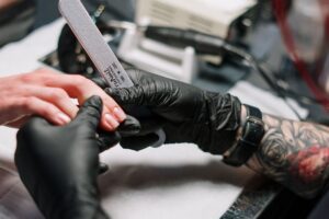 Nail technician wearing gloves filing a client's nails during a manicure