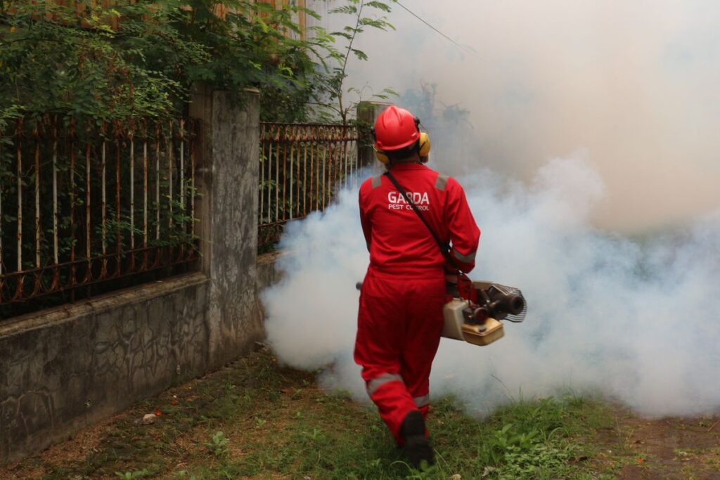 Pest control technician fogging an outdoor area around a home to treat pests