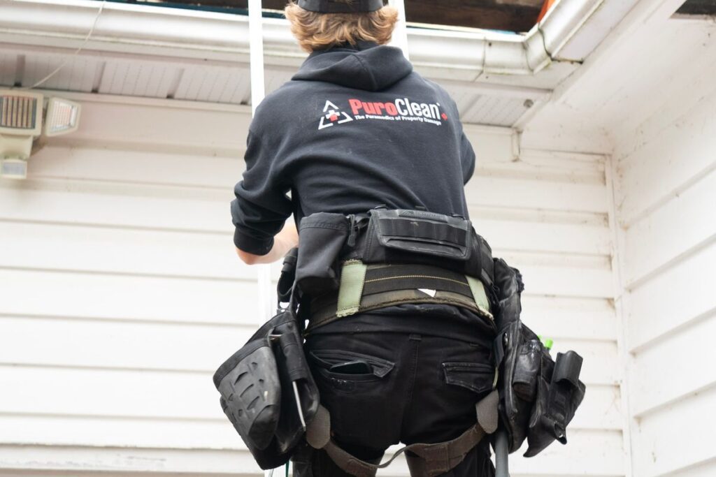 Professional roofer climbing a ladder to inspect a roof near a chimney