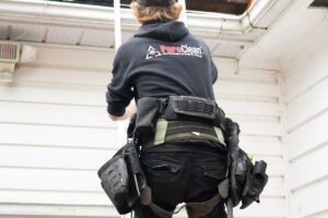 Professional roofer climbing a ladder to inspect a roof near a chimney