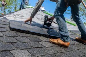 Roofer using a nail gun to fix asphalt shingles onto a new residential roof