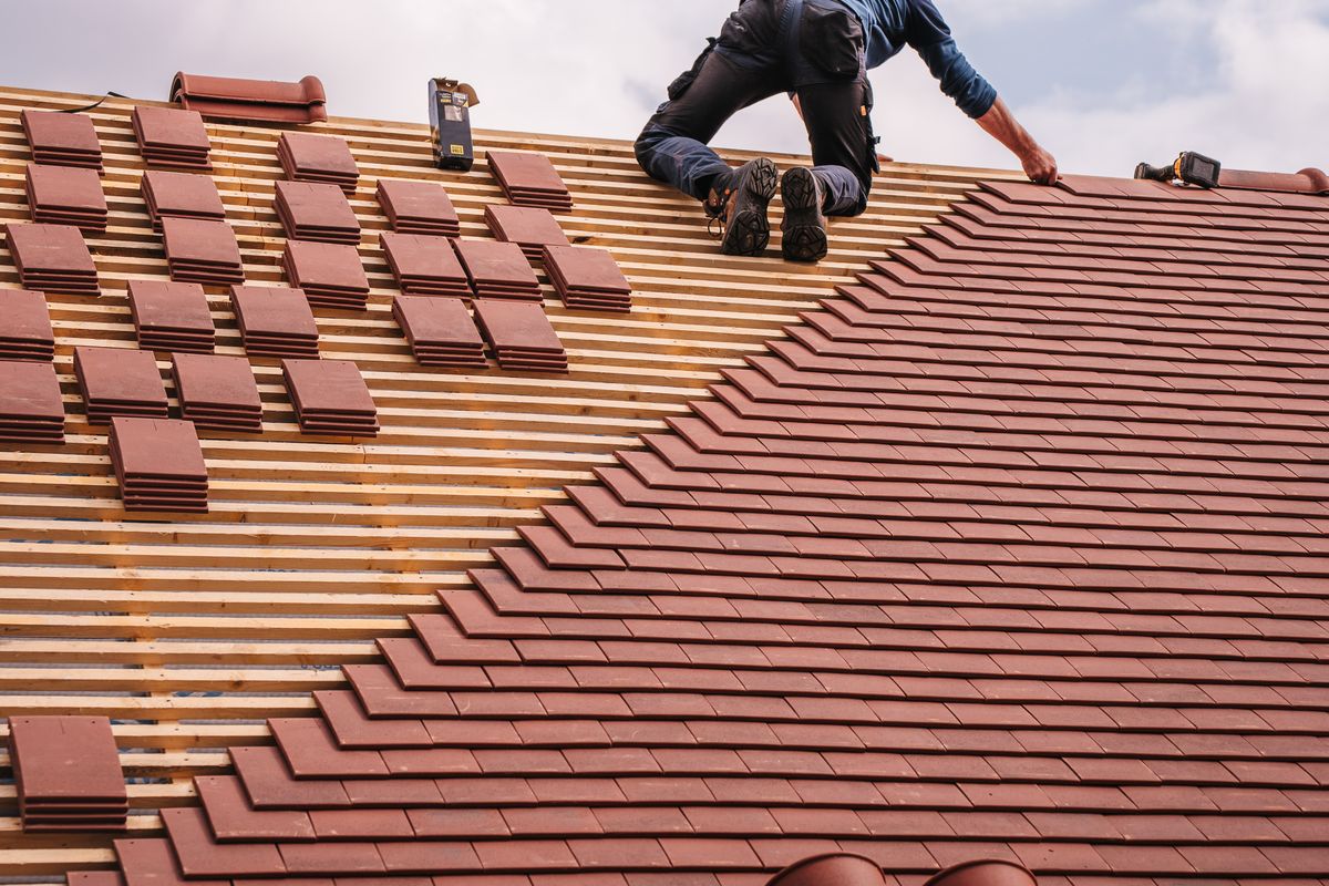Roofer carefully laying rows of shingles across a newly decked roof