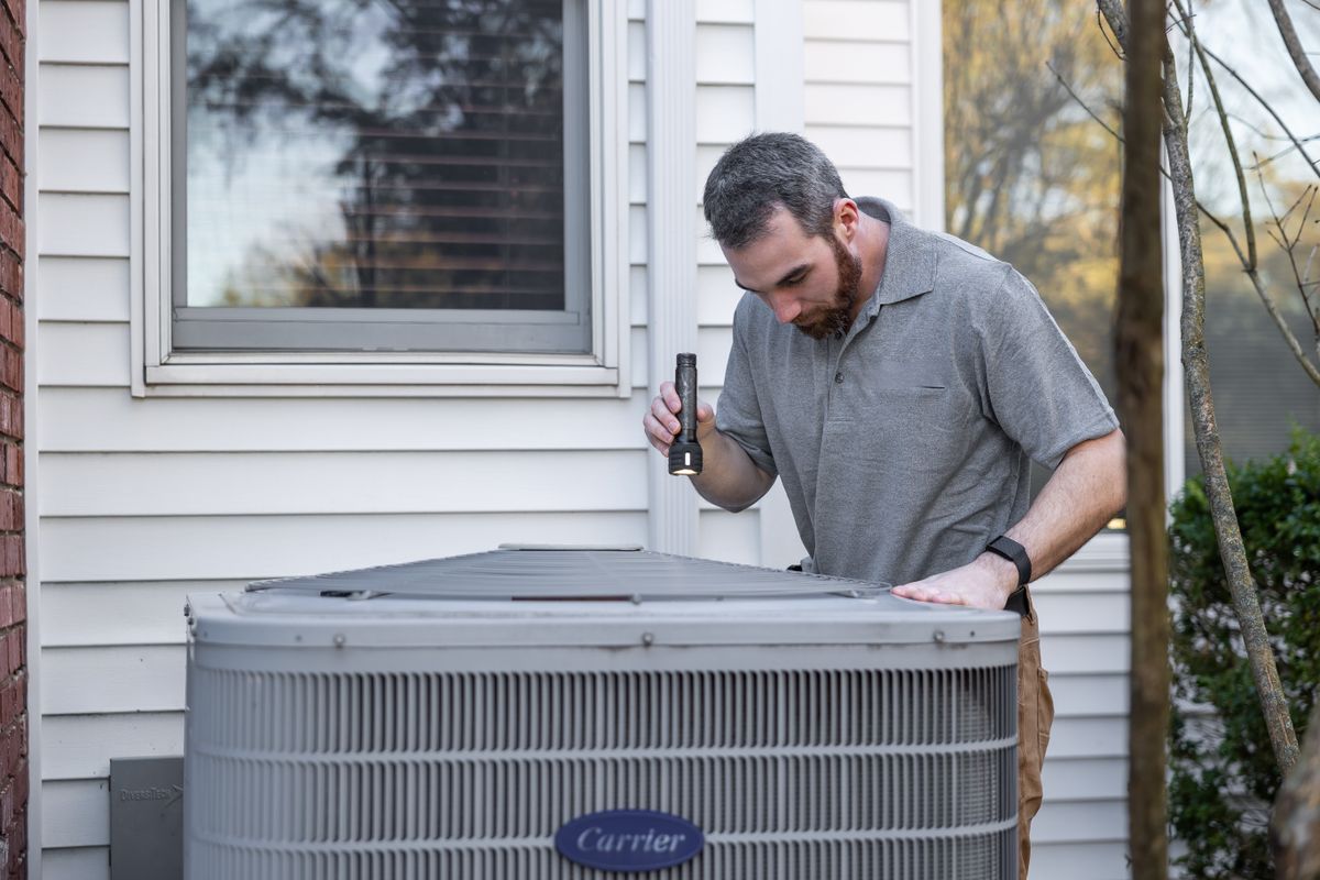 Technician inspecting the coils and casing of an outdoor HVAC condenser unit