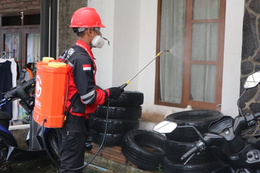 Pest control technician in safety gear applying treatment along a building exterior