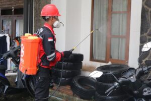 Pest control technician in safety gear applying treatment along a building exterior