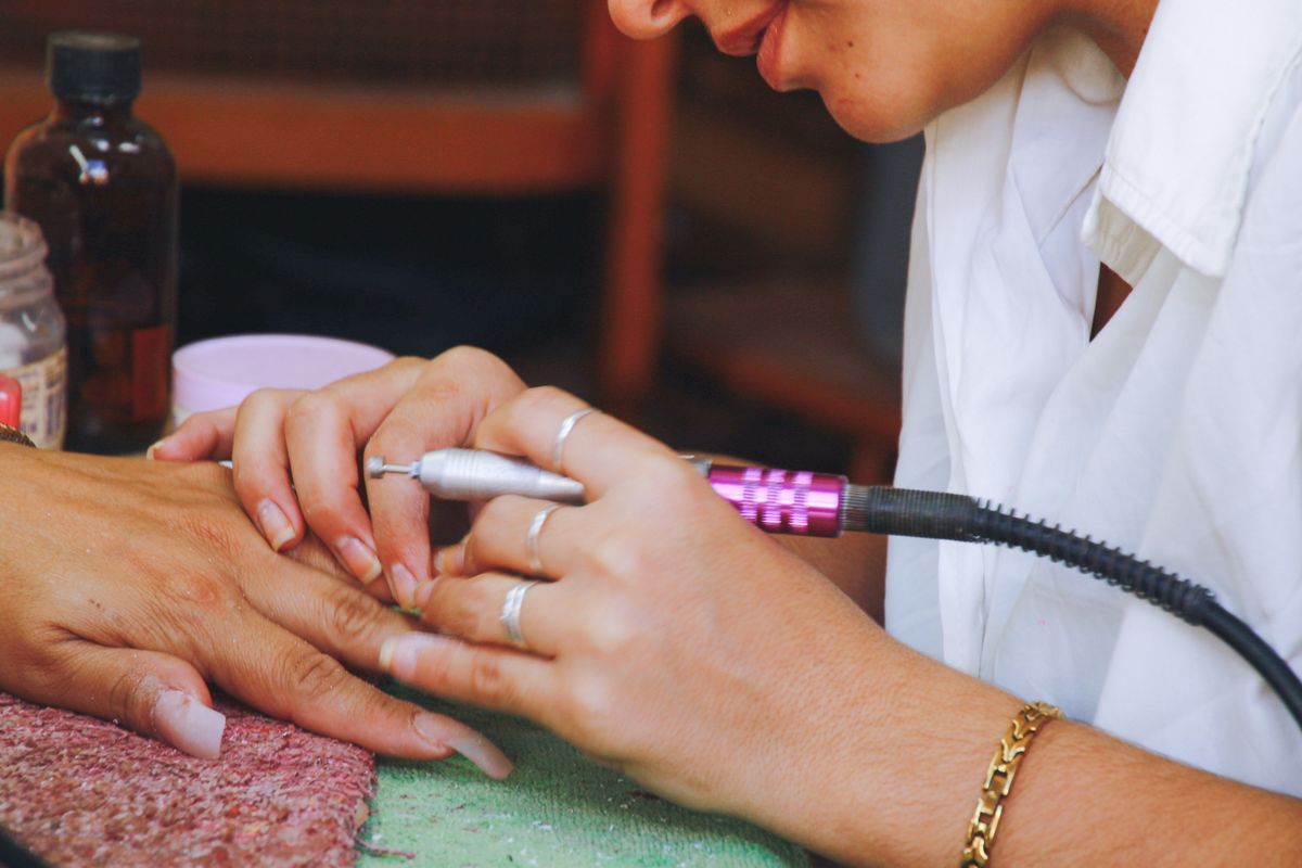 Nail technician using an electric file during a manicure appointment