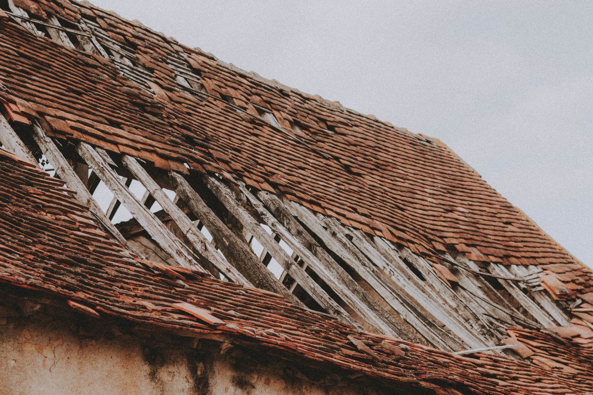 Close-up of an ageing roof with missing shingles and exposed timber beneath